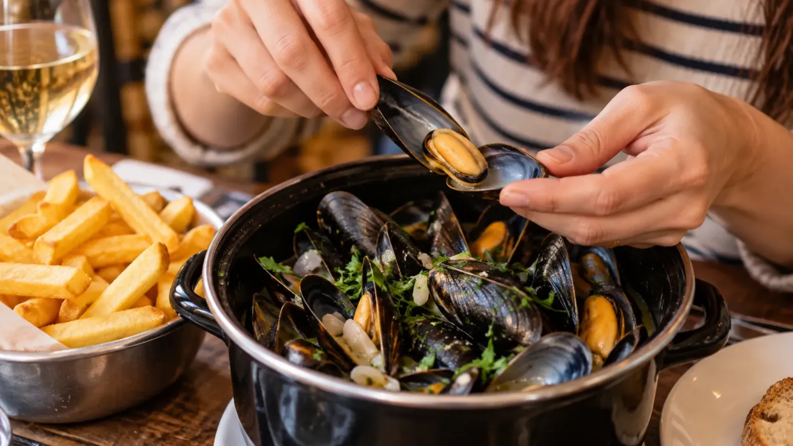 Cận cảnh thực khách dùng vỏ trai rỗng để gắp thịt trai trong bữa Moules-frites, bên cạnh có khoai tây chiên