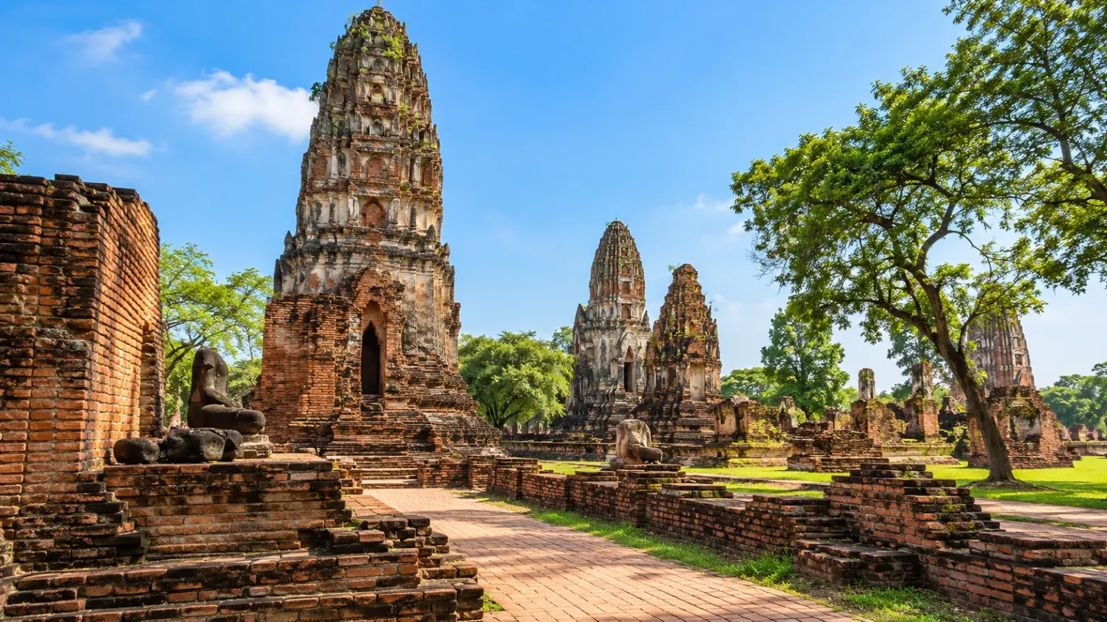 Khu di tích Wat Mahathat ở Ayutthaya với tháp gạch cổ, tường đổ nát và lối đi giữa các công trình lịch sử.