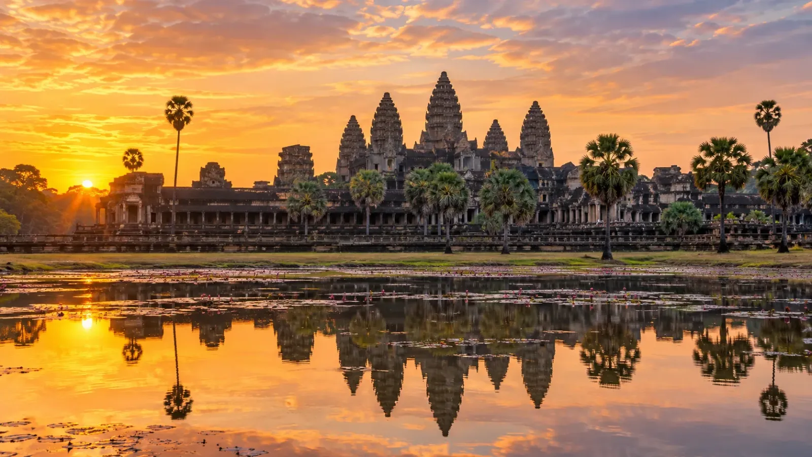 Quần thể đền Angkor Wat tại Campuchia trong ánh sáng bình minh, với các ngọn tháp Khmer và mặt nước phía trước.