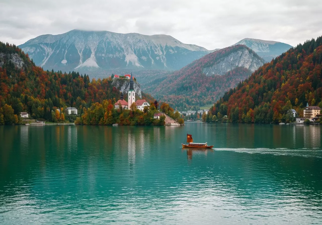 Hồ Bled ở Slovenia với nhà thờ trên đảo và lâu đài trên vách đá, bao quanh bởi rừng cây mùa thu