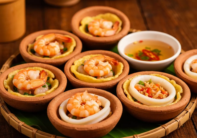 Những chiếc bánh căn nhỏ xinh với nhân tôm và mực đang được nướng trong khuôn đất nung truyền thống, ăn kèm nước chấm đặc trưng, tạo nên một món ăn vặt hấp dẫn